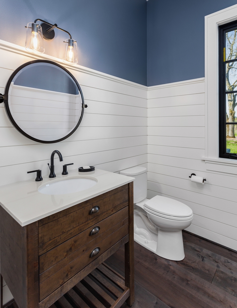 Bathroom in luxury farmhouse style home with vanity, circular mirror, black faucet, sink, and hardwood floor.